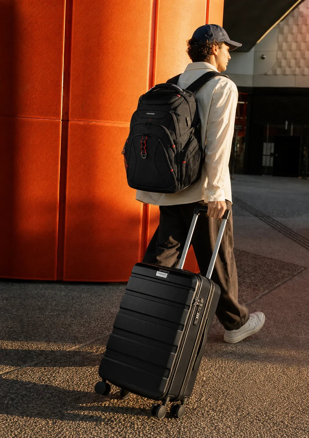 Traveler carrying a black KROSER laptop backpack and rolling a black carry-on suitcase