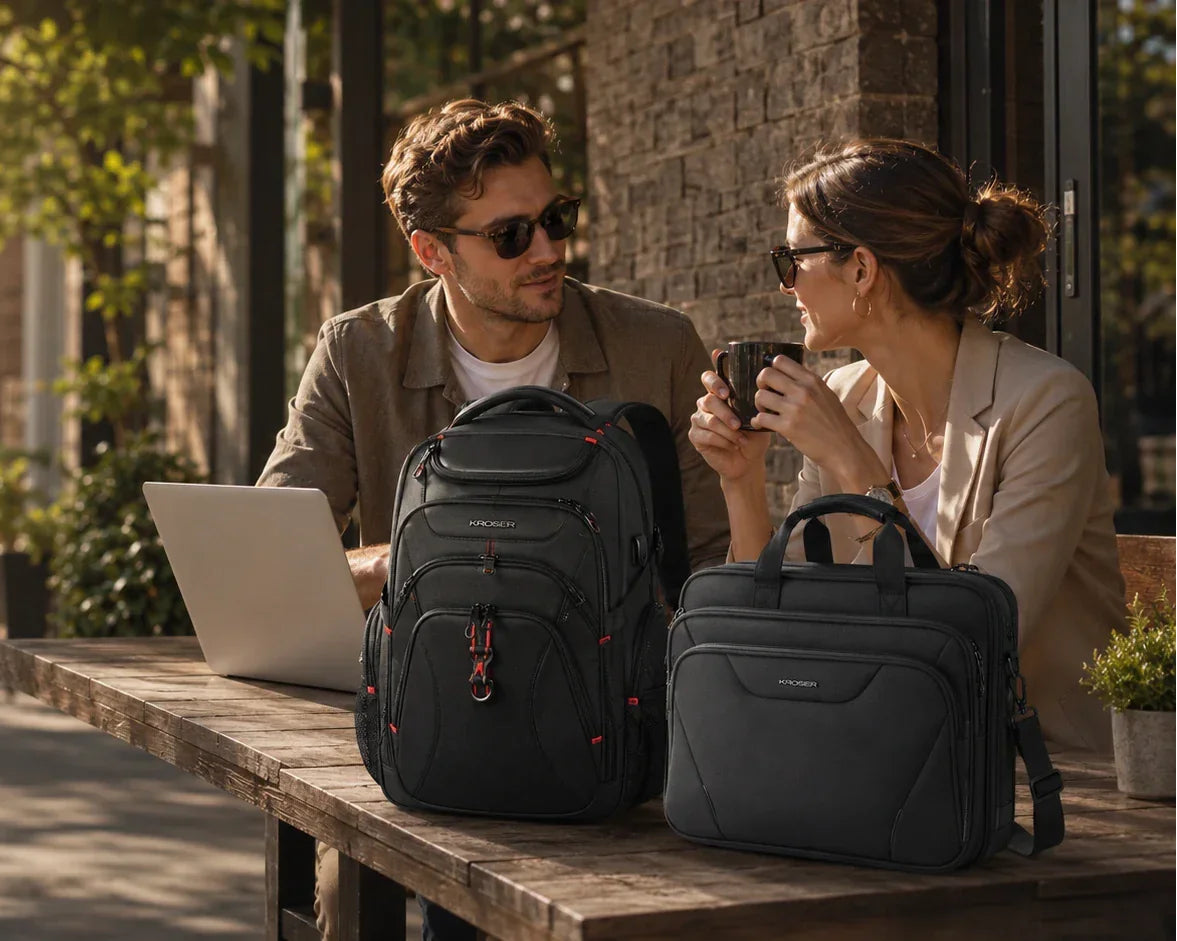 A man and a woman sitting at an outdoor cafe table with a black Kroser backpack and a matching black briefcase placed in the foreground.